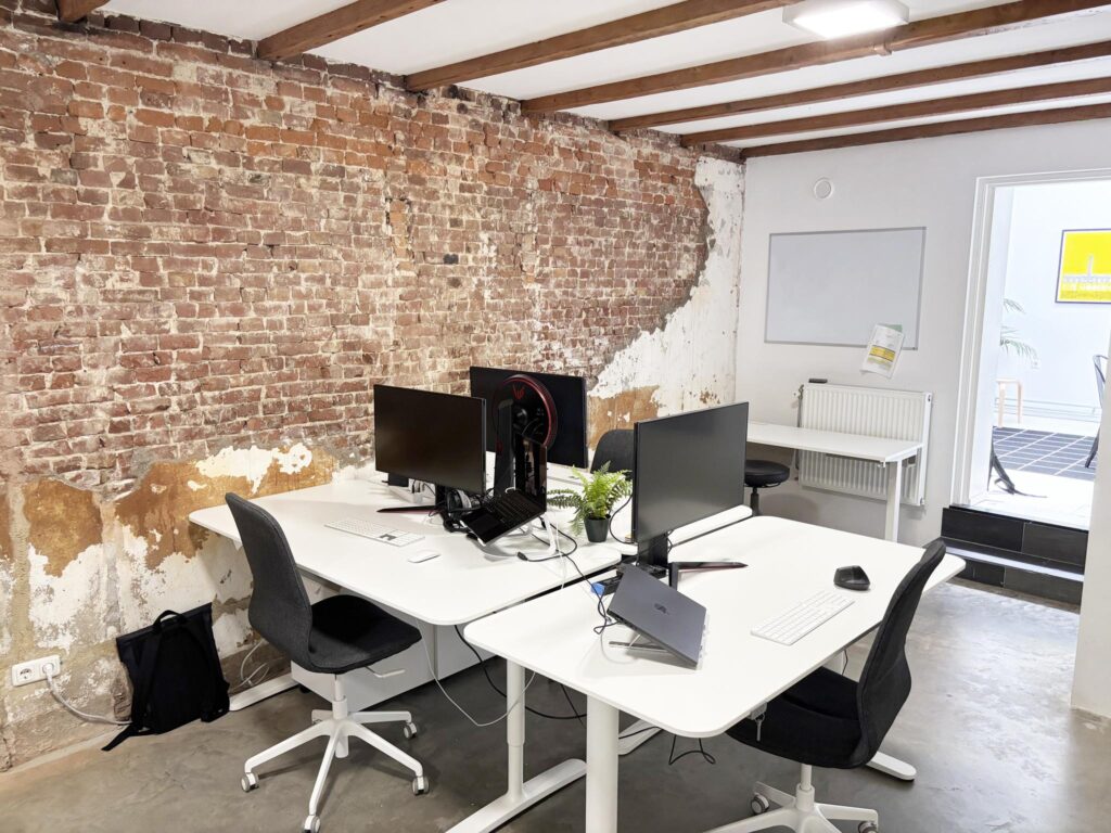Modern office workspace with white desks, black chairs, and exposed brick wall on Van Ostadestraat.